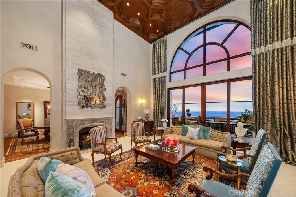 Living room with a stone fireplace, coffered wood ceiling, and tall ocean-facing windows at dusk.