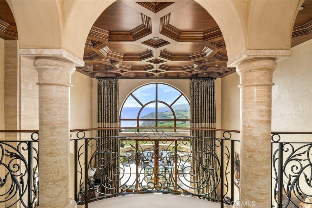 Interior landing with a coffered wood ceiling, stone columns, and an arched window overlooking the coast.