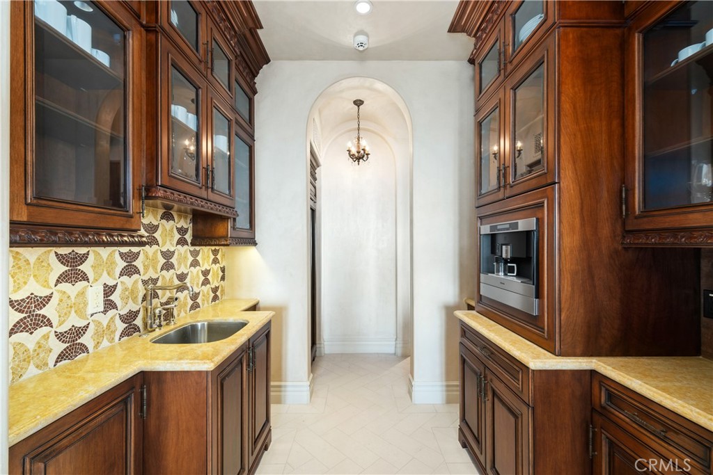 Kitchen with dark wood cabinetry, patterned tile backsplash, golden counters, and built-in coffee maker.
