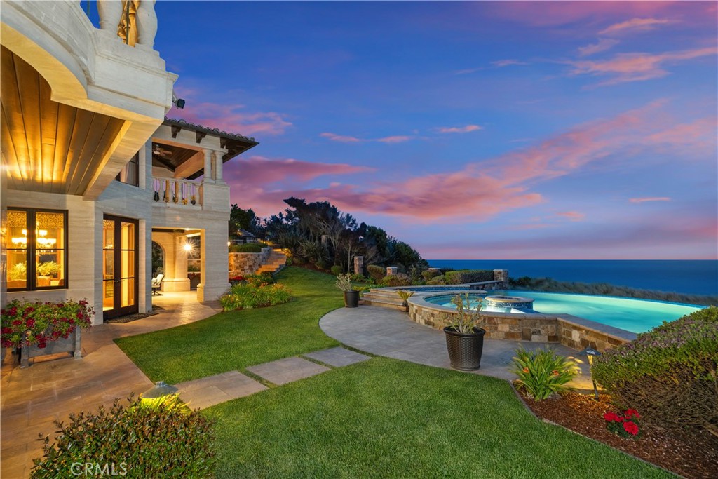 Coastal home and illuminated pool overlooking the ocean beneath a pink dusk sky.