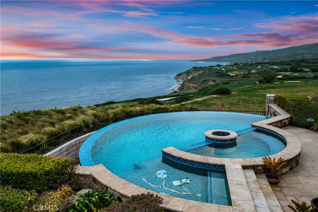 Curved swimming pool and raised spa overlooking the ocean and coastline at dusk.
