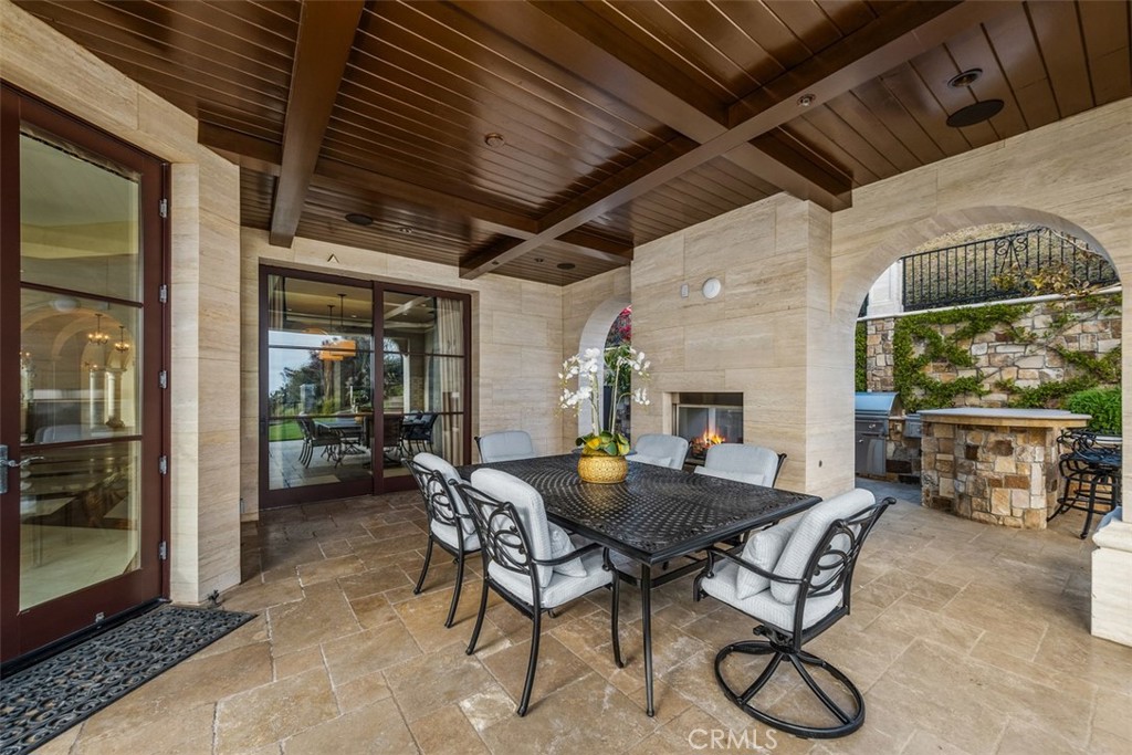 Covered patio with a wood-beamed ceiling, outdoor dining table, and stone fireplace.