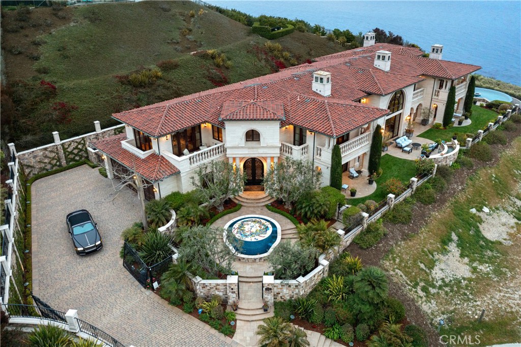 Coastal home with red-tile roofs, circular pool, and ocean behind.