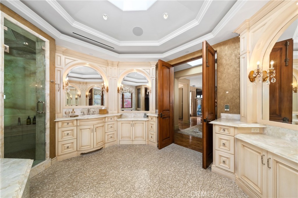 Bathroom with cream cabinetry, marble counters, arched mirrors, and a glass-enclosed shower.