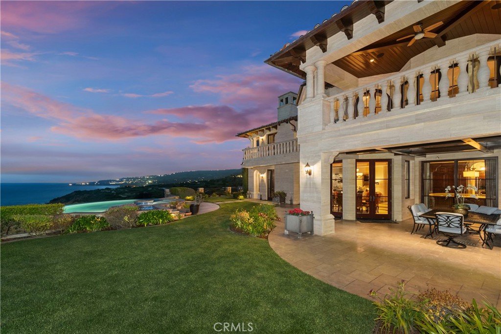 Ocean-facing home with a covered terrace, lawn, and pool overlooking the coast at dusk.