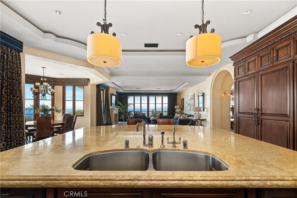 Kitchen with a broad stone island, double sink, dark wood cabinetry, and ocean views through the windows.
