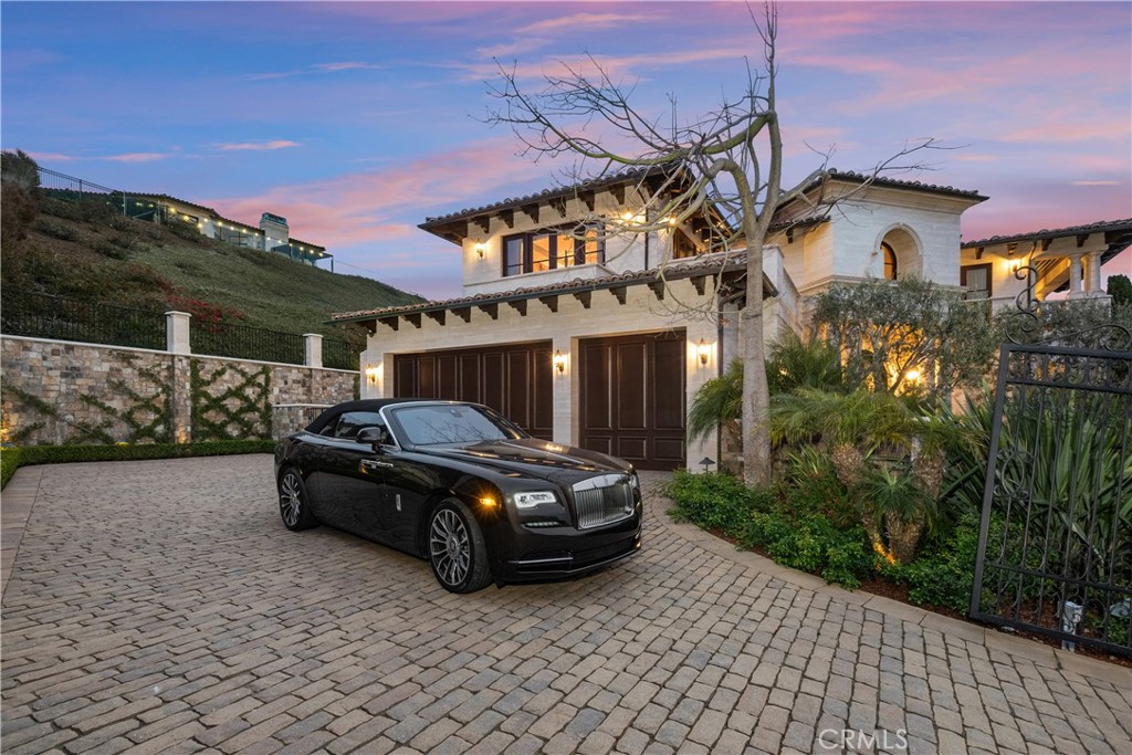 Two-story stucco home with twin garage doors and a black car on the cobblestone drive.
