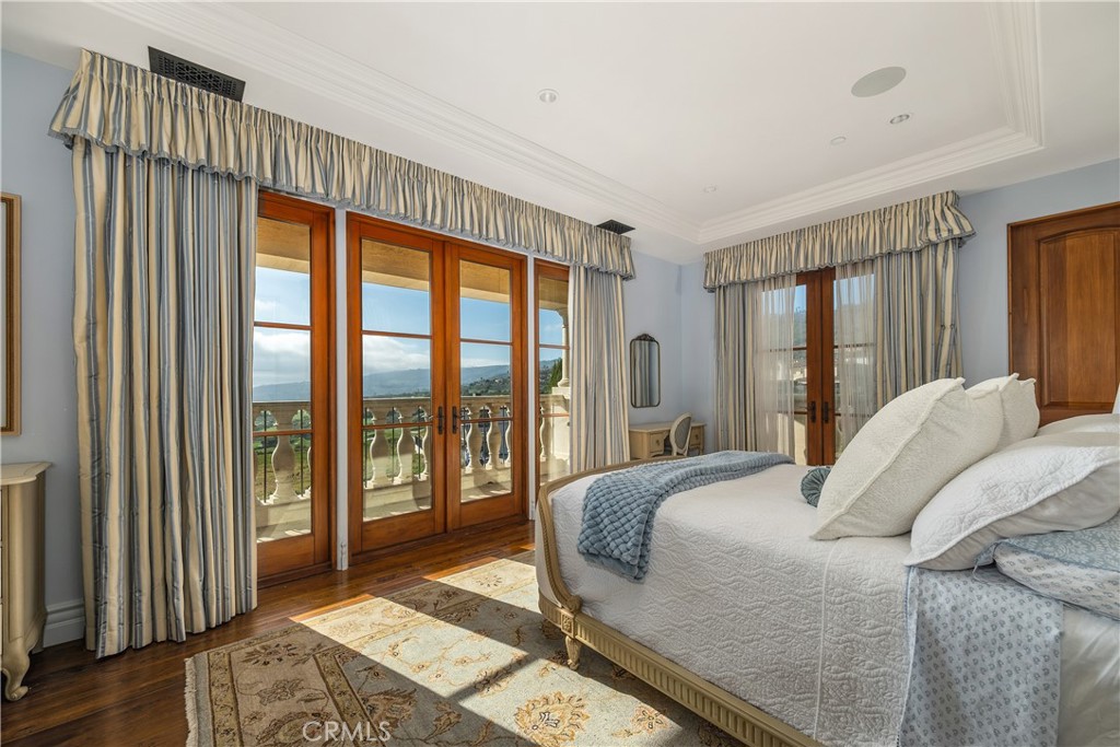 Bedroom with a white bed and wood-framed balcony doors overlooking the coast.
