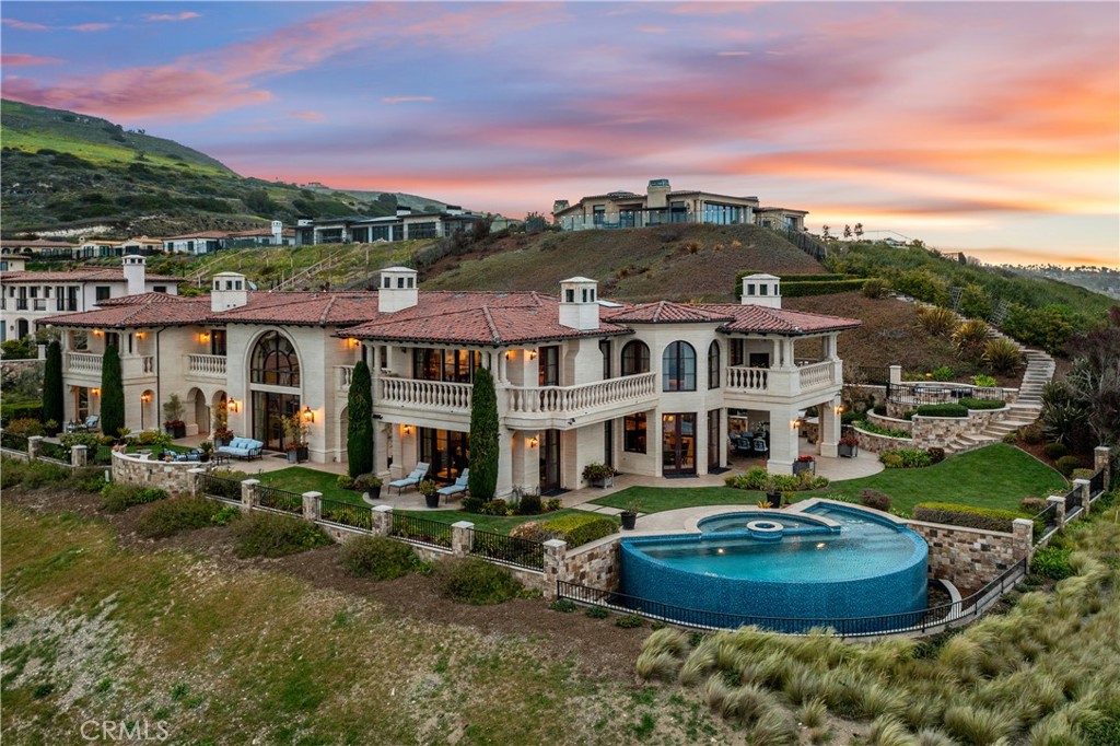Mediterranean-style hillside home with red tile roof and circular pool at sunset