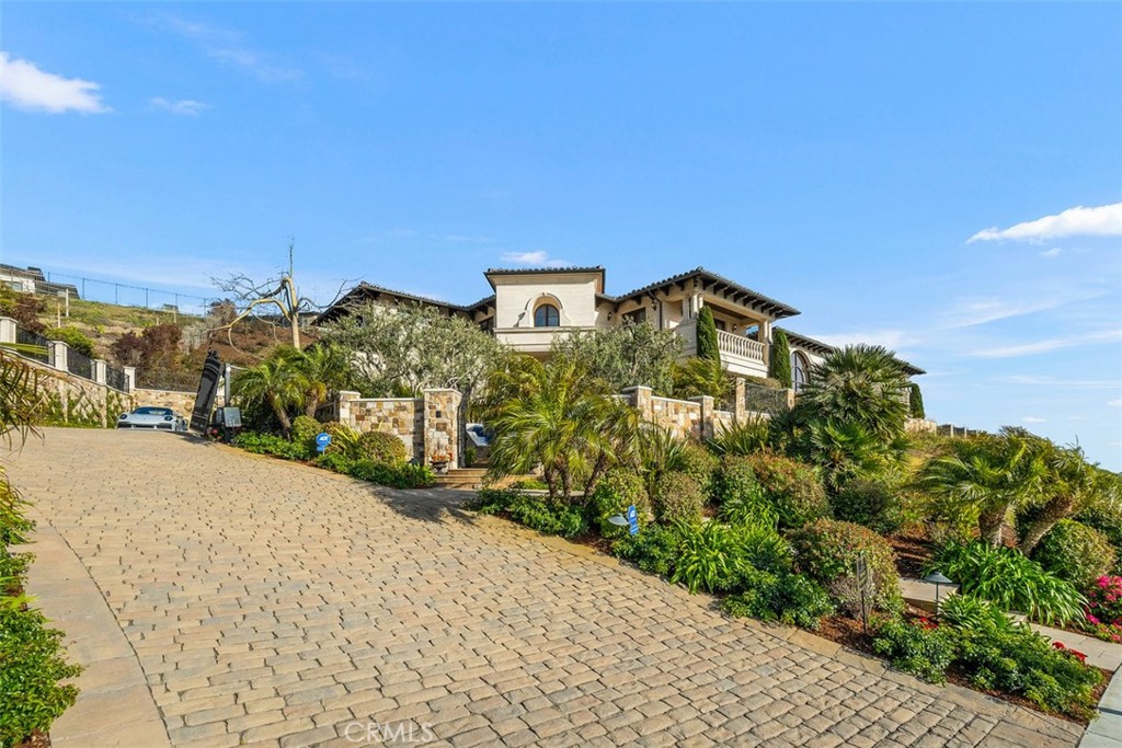 Mediterranean-style hillside home above a broad paved driveway and landscaped stone walls.