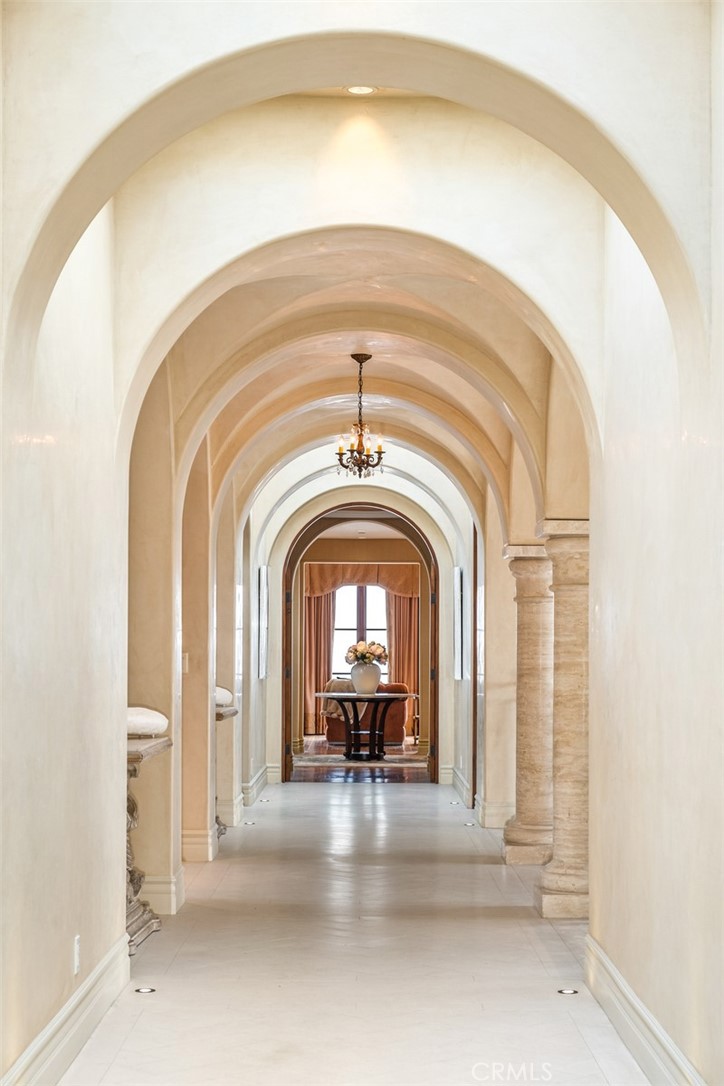 Arched hallway with stone columns, a chandelier, and a flower-topped console table.