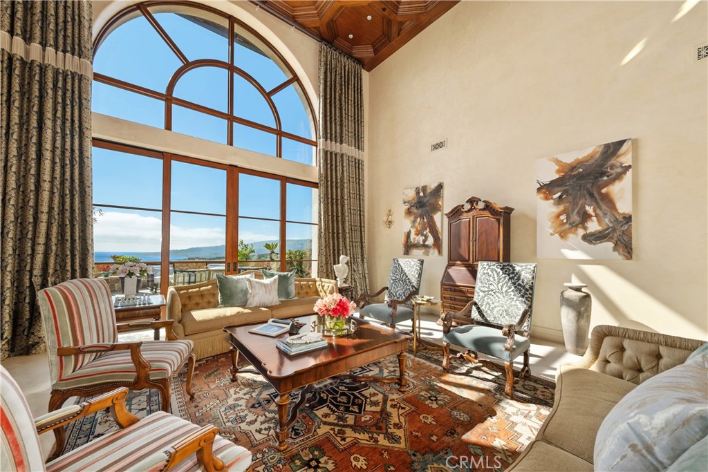 Living room with a soaring arched window overlooking the ocean, traditional furnishings, and a patterned rug.