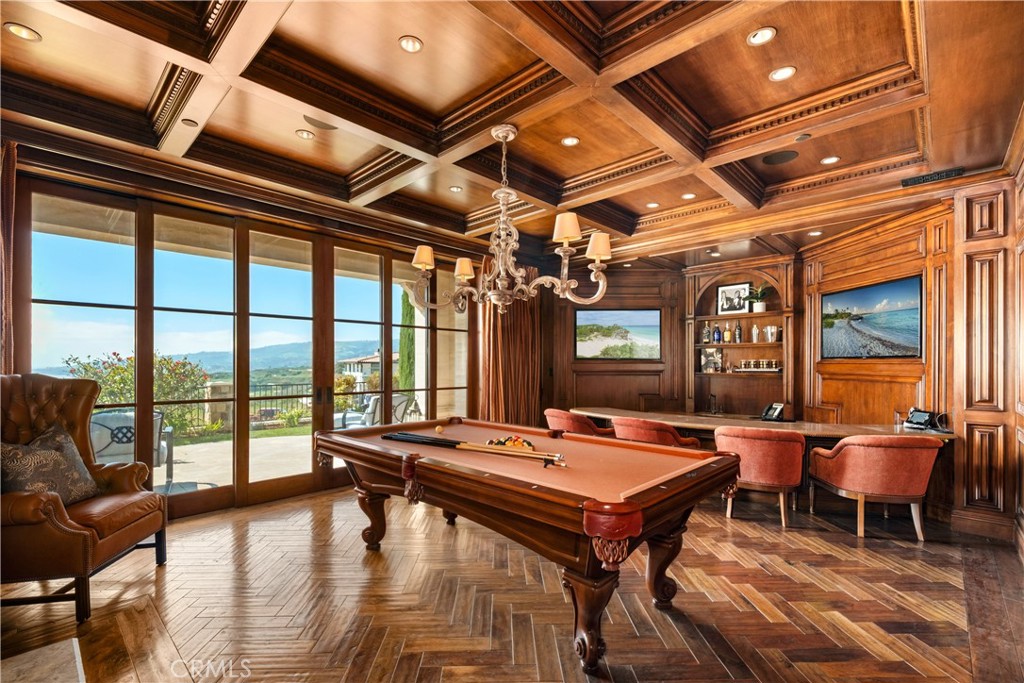 Wood-paneled billiard room with a pool table and sliding doors overlooking the coast.