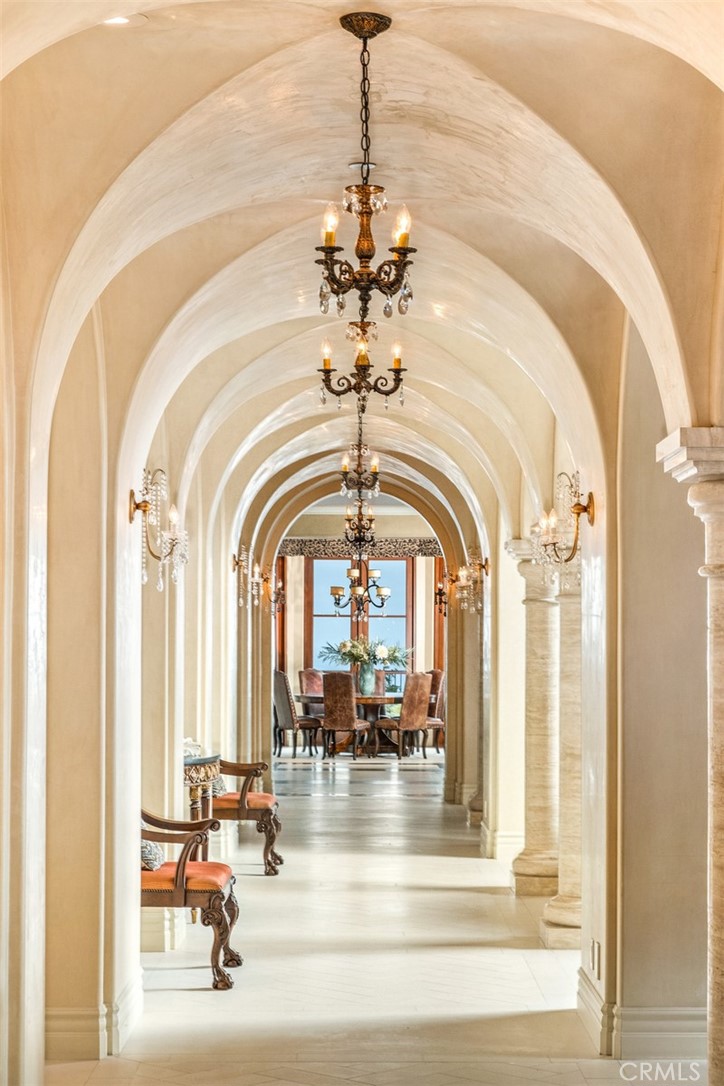 Arched hallway with ornate chandeliers, upholstered chairs, and a dining area at the far end.