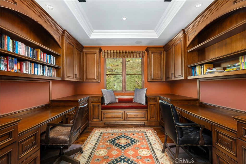 Wood-paneled home office with built-in bookshelves, dual desks, and a cushioned window seat.