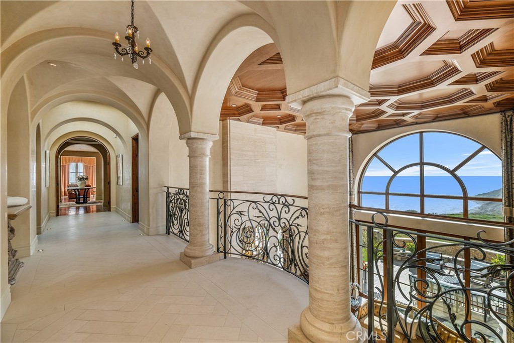Arched hallway with stone columns, ornate railings, coffered wood ceiling, and an ocean view.