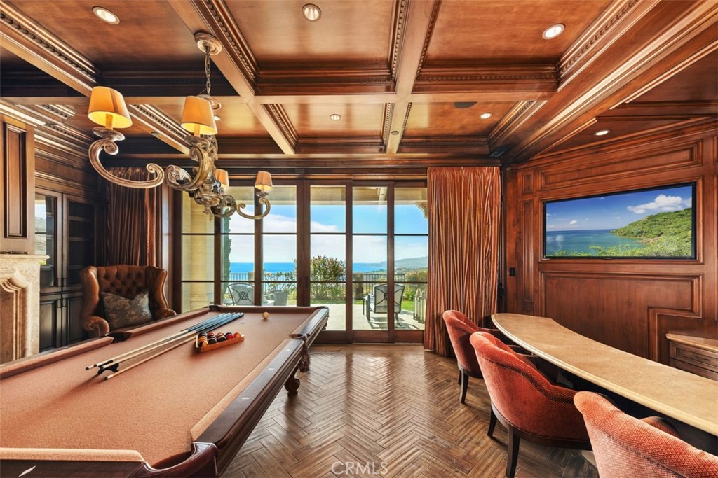 Billiard room with a pool table, rich wood paneling, and ocean views through sliding glass doors.