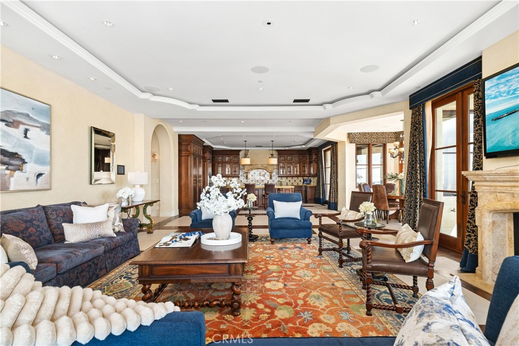 Living room with blue seating, ornate rug, stone fireplace, and an open kitchen with dark wood cabinets.