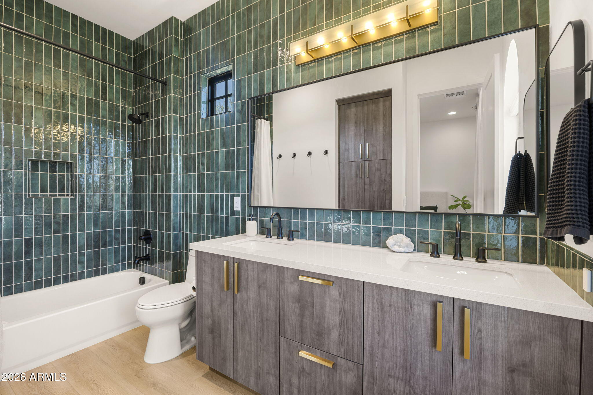 Bathroom with dark green tiled tub surround and a double-sink gray wood vanity.
