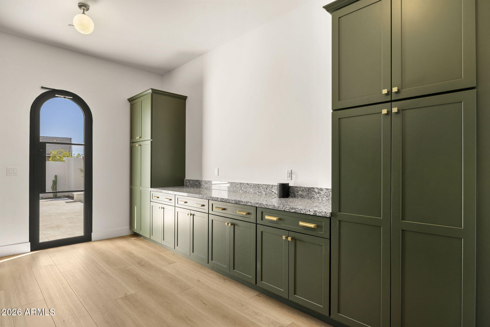 Kitchen with olive-green cabinetry, brass hardware, and an arched glass door to the patio.