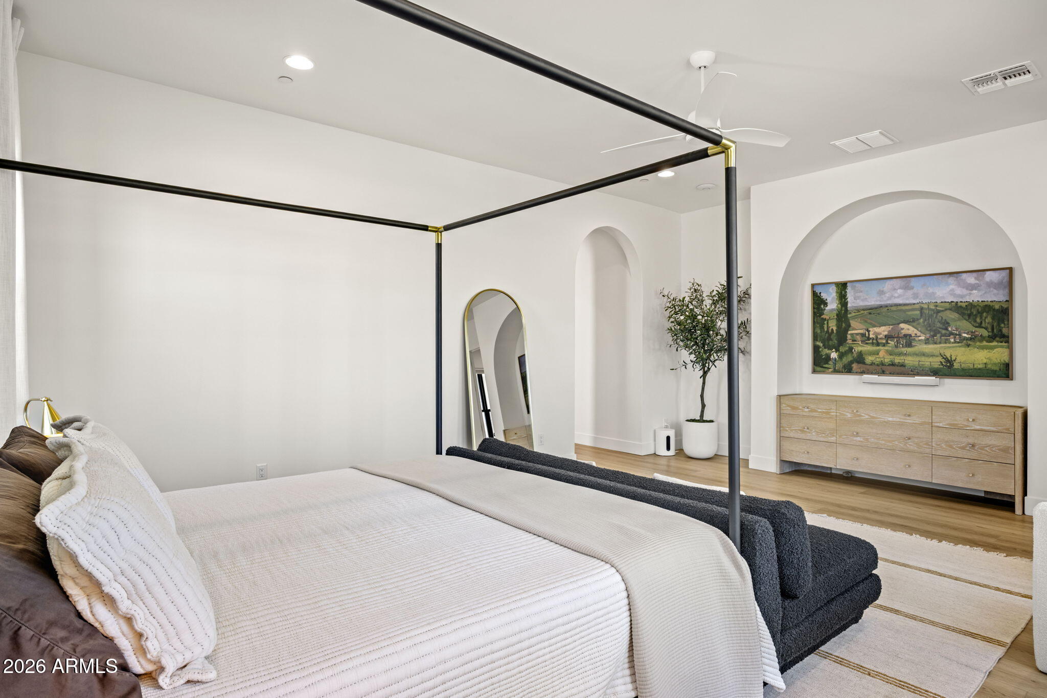 Furnished bedroom with a black four-poster bed, arched niche, and light wood dresser.