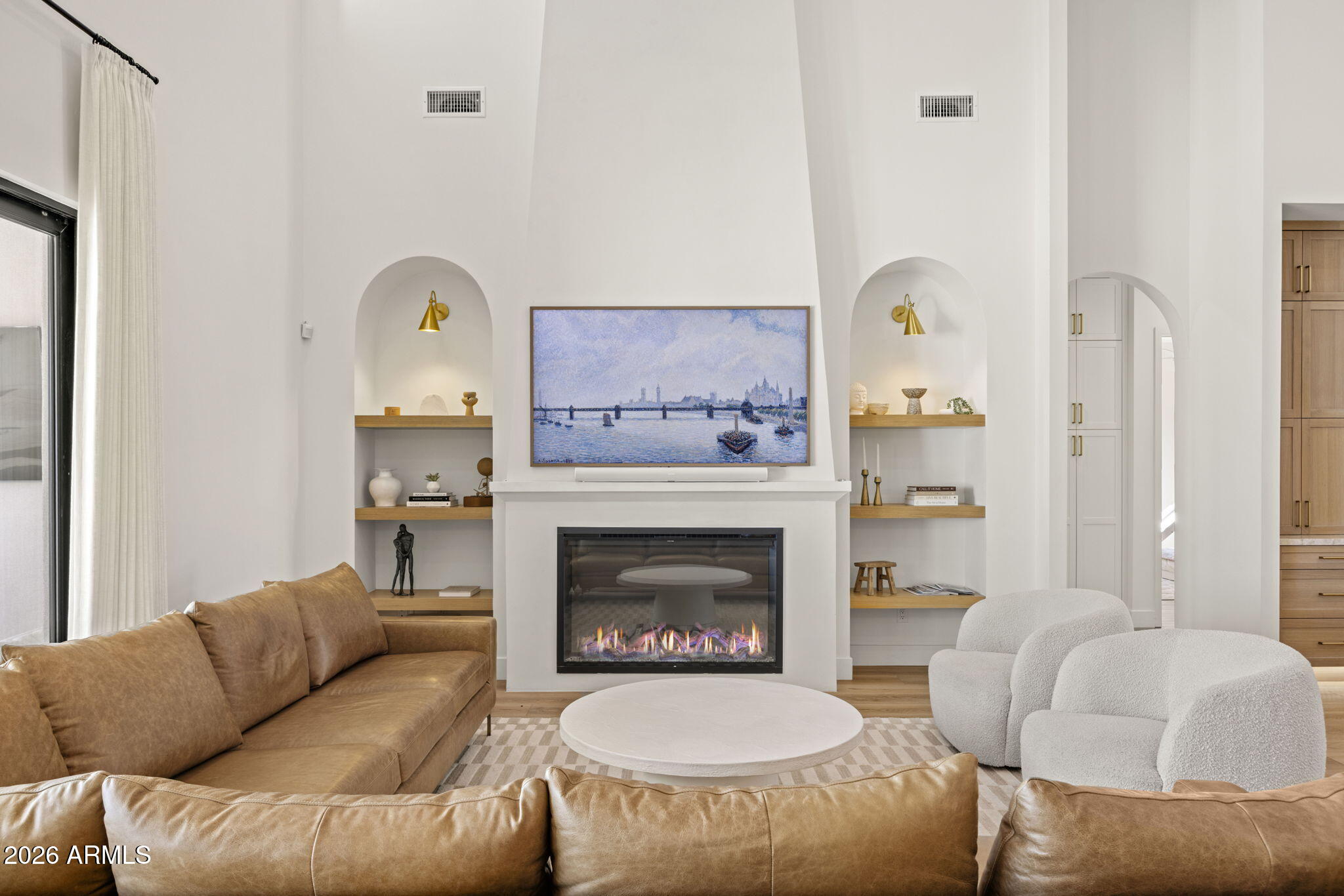 Living room with a tall white fireplace, built-in shelves, tan sectional, and white boucle chairs.