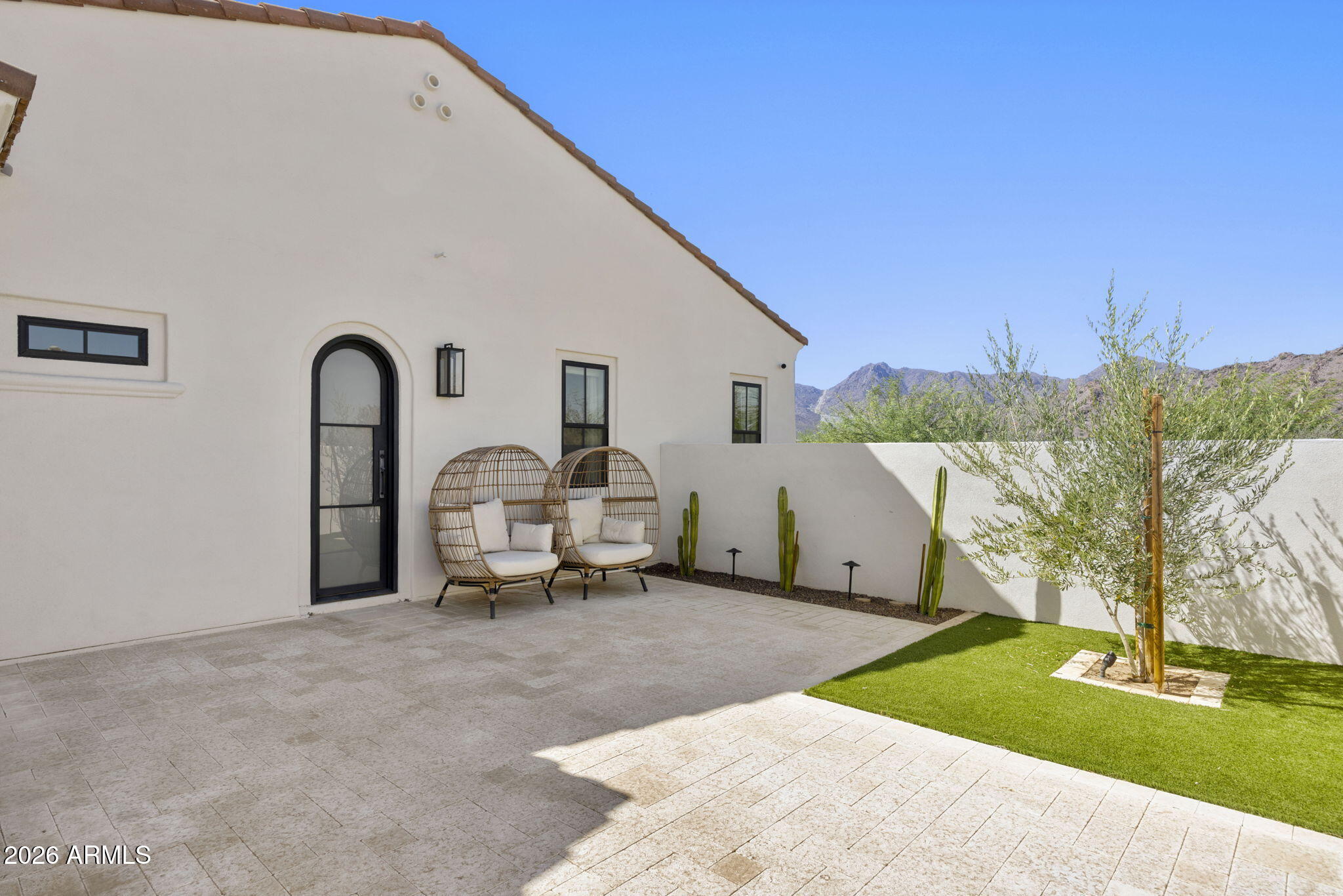 Back patio with woven lounge chairs, paver terrace, desert landscaping, and mountain views.