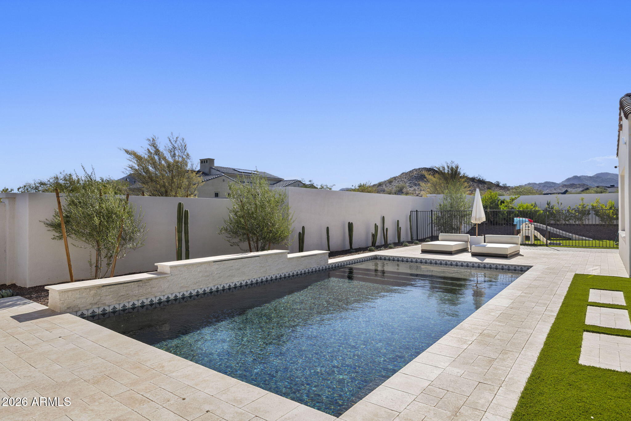 Backyard pool and stone patio with lounge chairs, desert landscaping, and mountains beyond the wall.