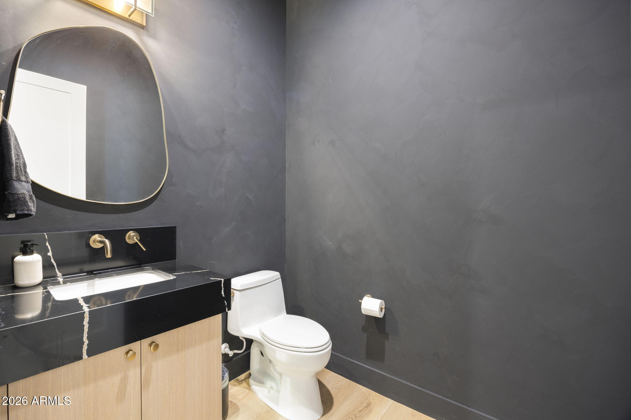 Bathroom with charcoal walls, a veined black vanity, brass fixtures, and an arched mirror.