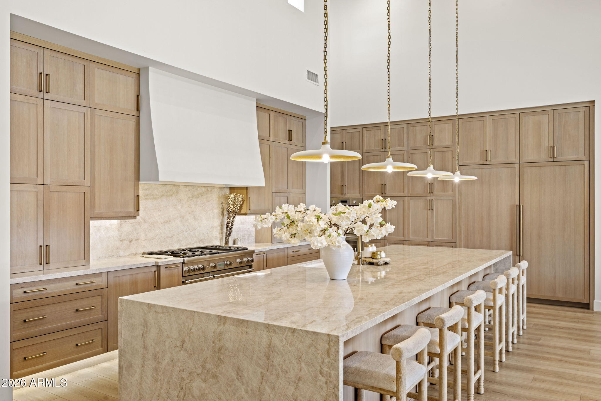 Kitchen with light wood cabinets, a marble island, upholstered stools, and pendant lights.