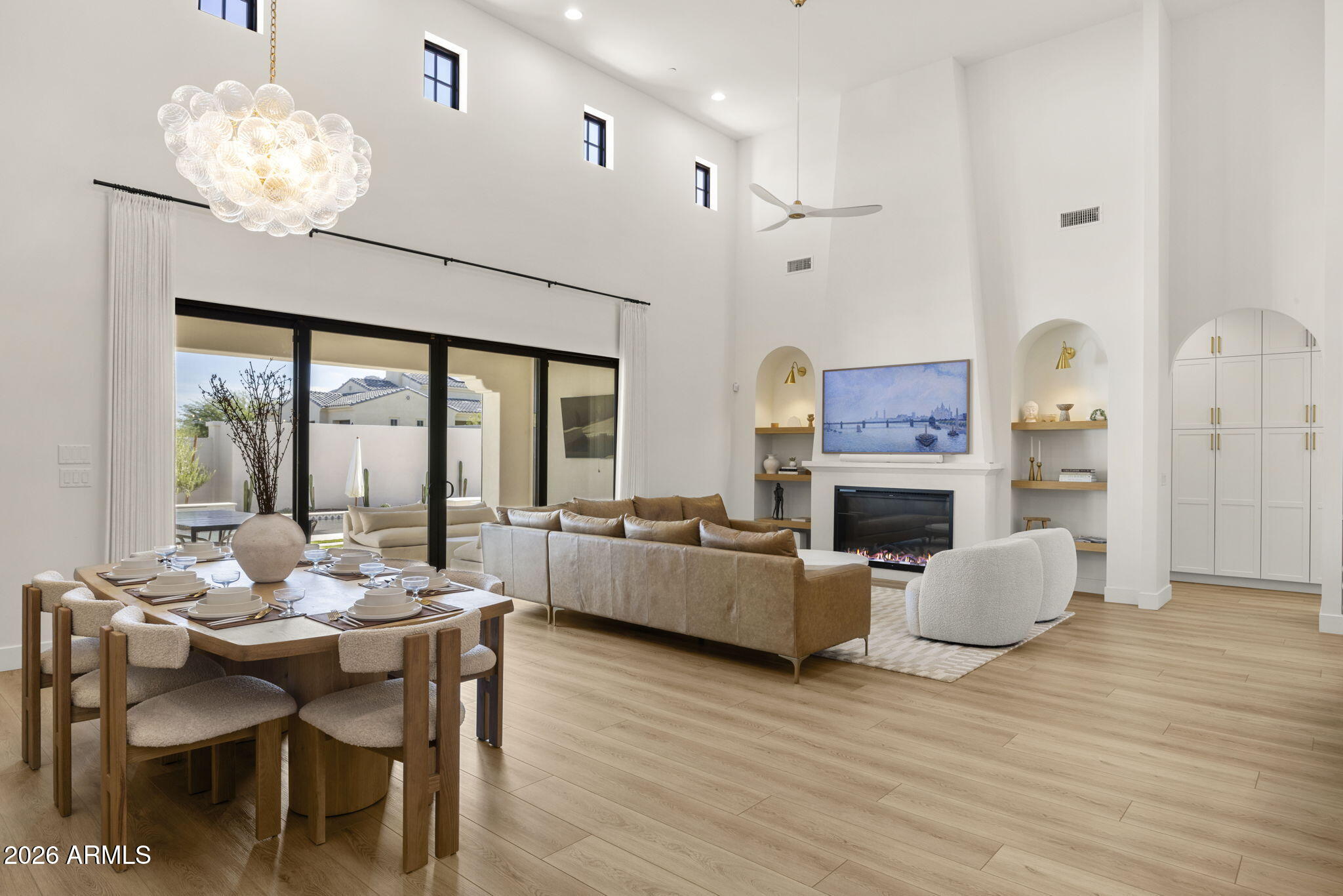 Double-height great room with dining area, glass chandelier, fireplace, and sliding doors to a patio.
