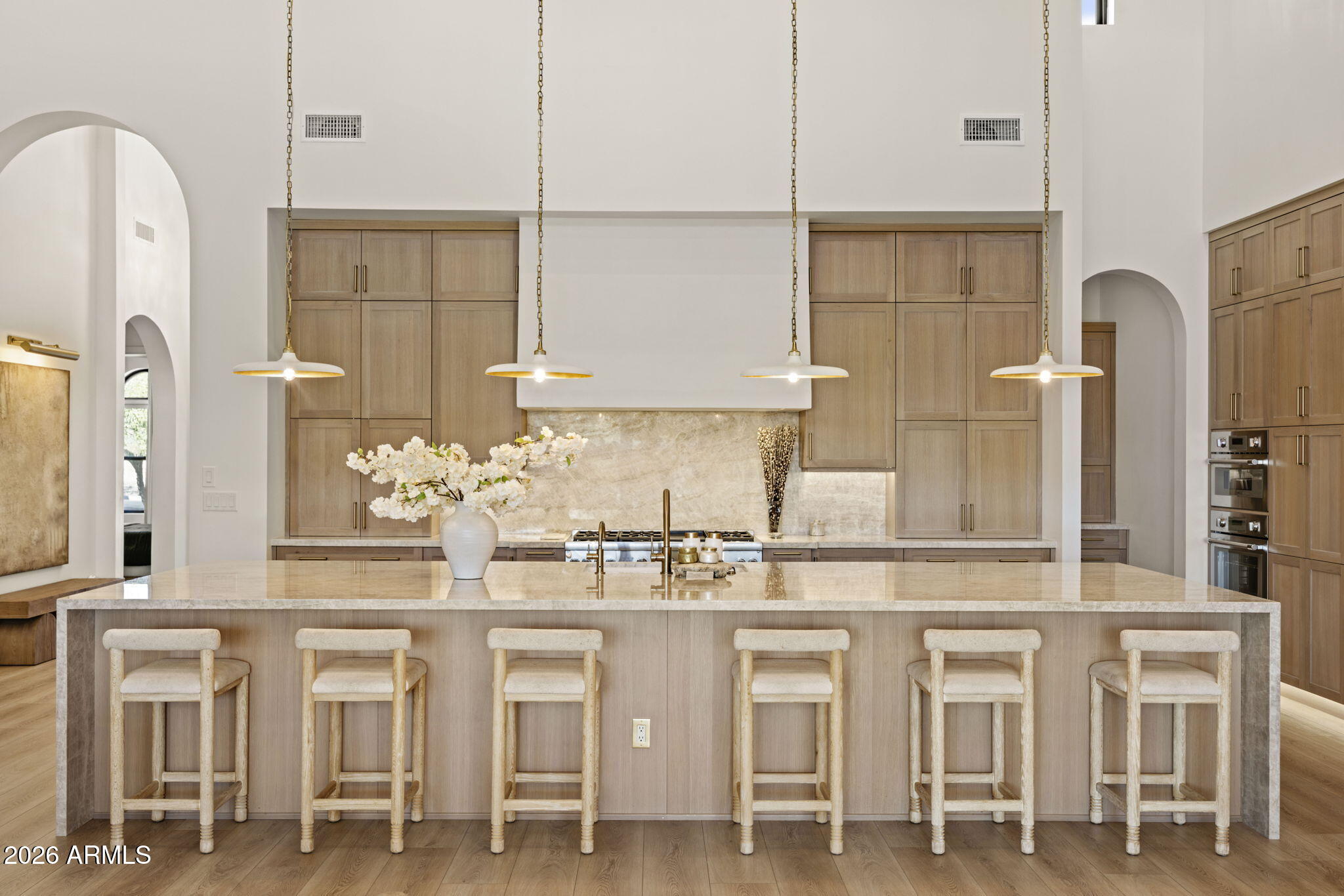 Kitchen with a large stone island, six stools, light wood cabinetry, and four pendant lights.