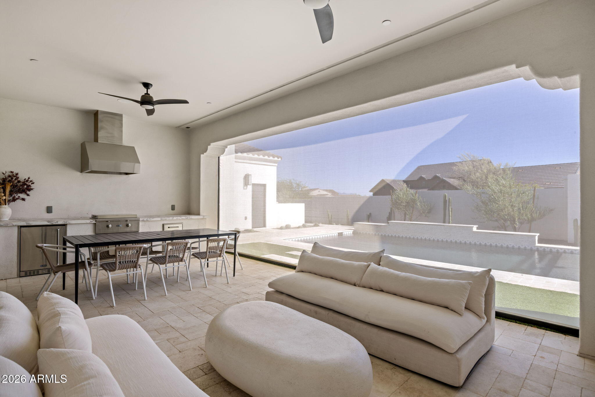 Covered patio with an outdoor kitchen and dining area, cushioned seating, and a pool view.