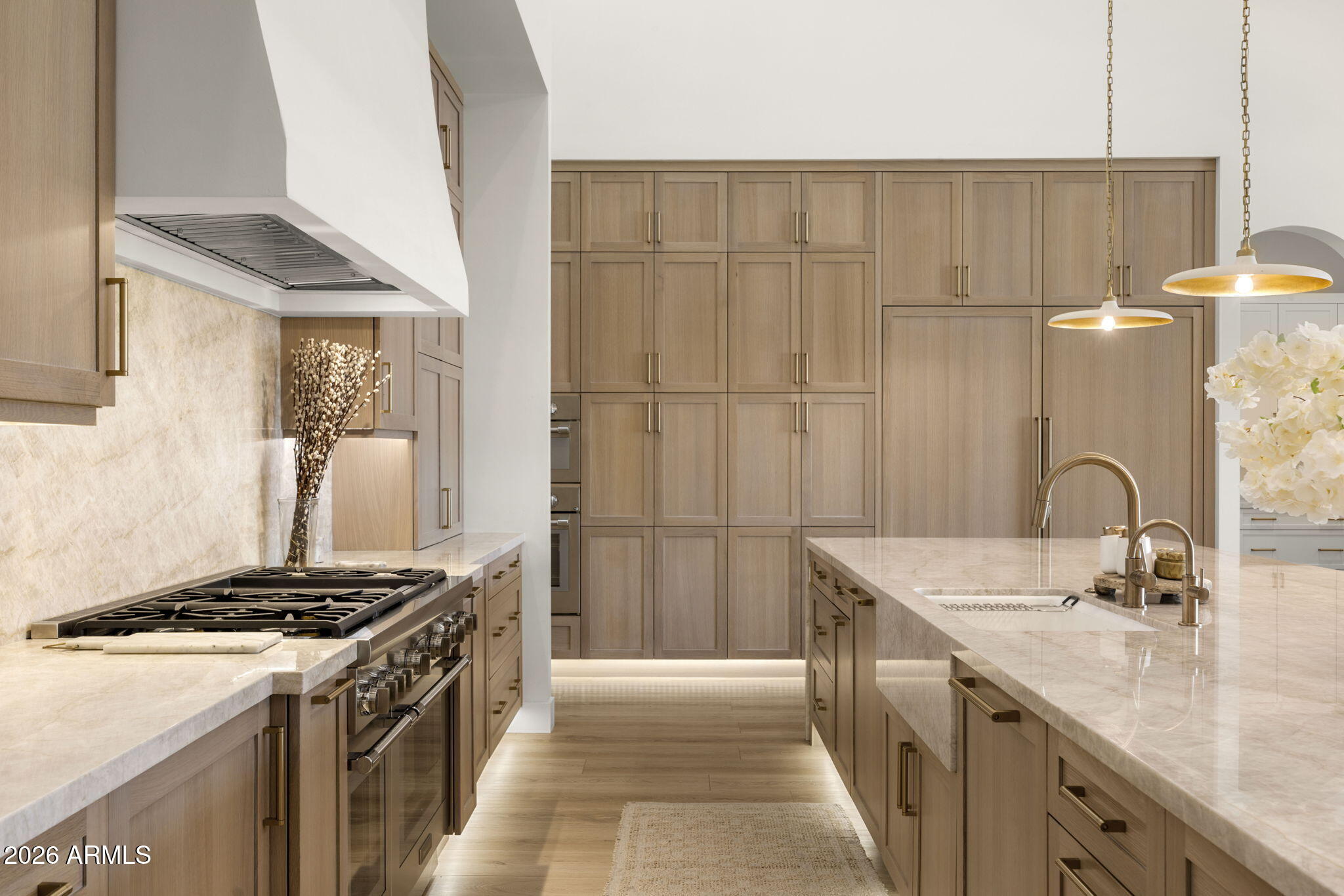 Kitchen with light wood cabinetry, pale stone island, brass fixtures, and a professional range.
