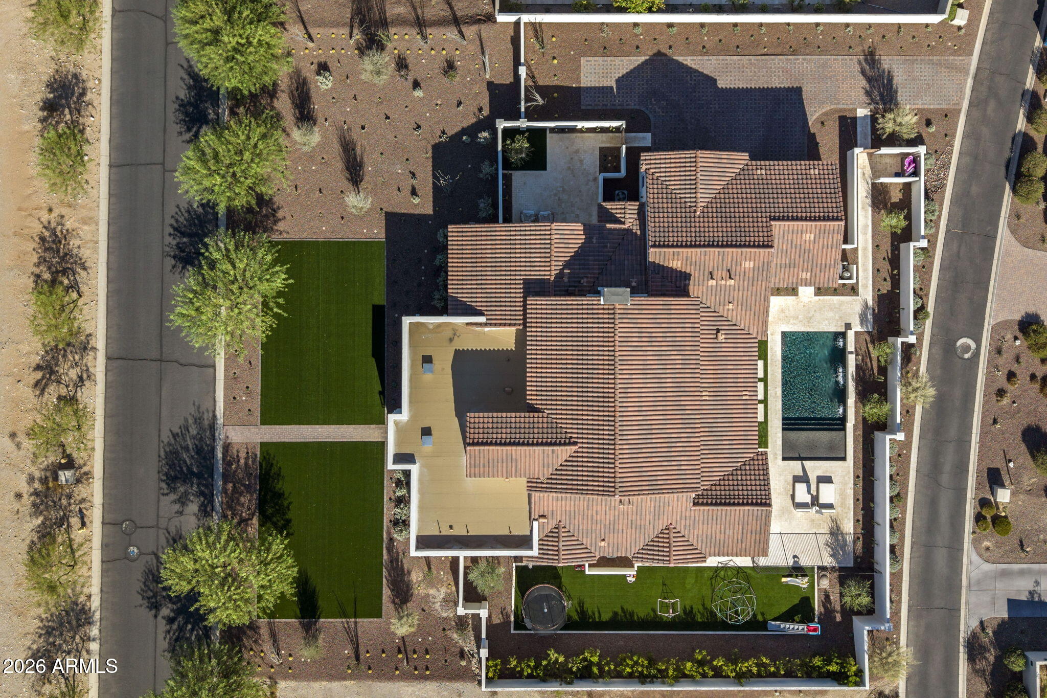 Aerial view of a tiled-roof home with a backyard pool, turf, and desert landscaping.