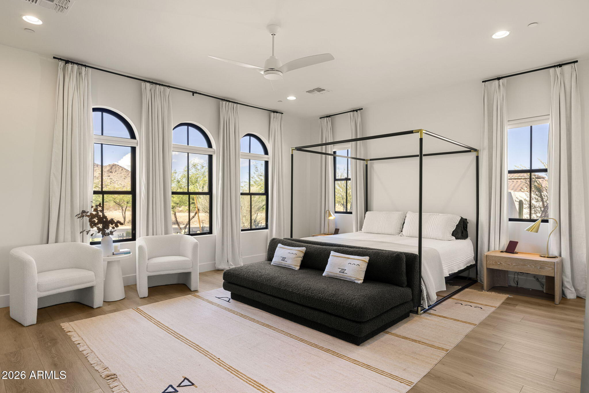 Bedroom with a black four-poster bed, arched windows, and desert foothills outside.