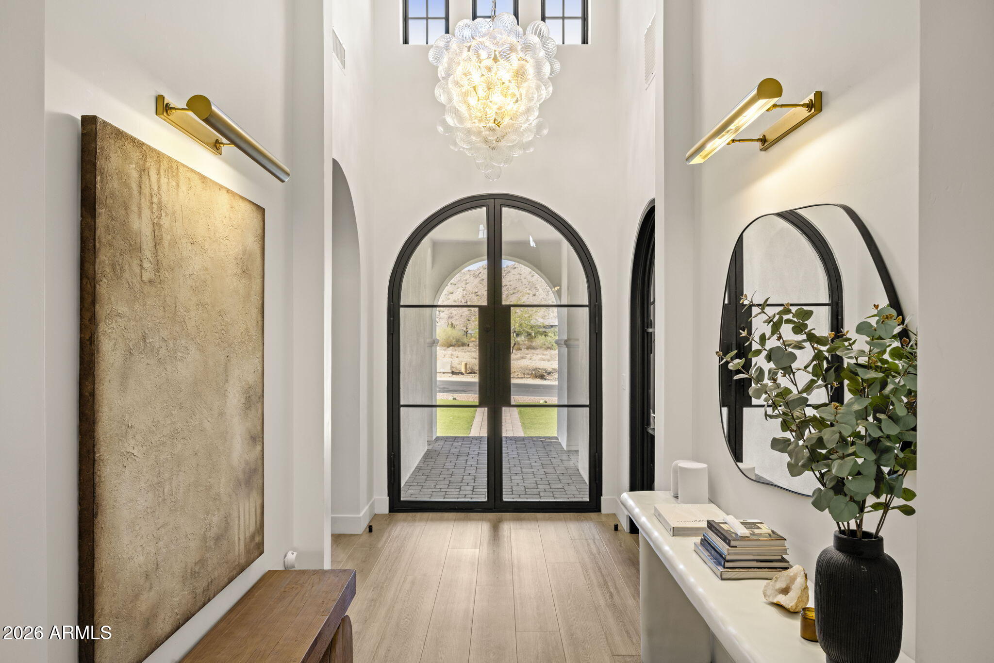 Entry foyer with an arched black-framed glass door, sculptural chandelier, and view of a desert hillside.