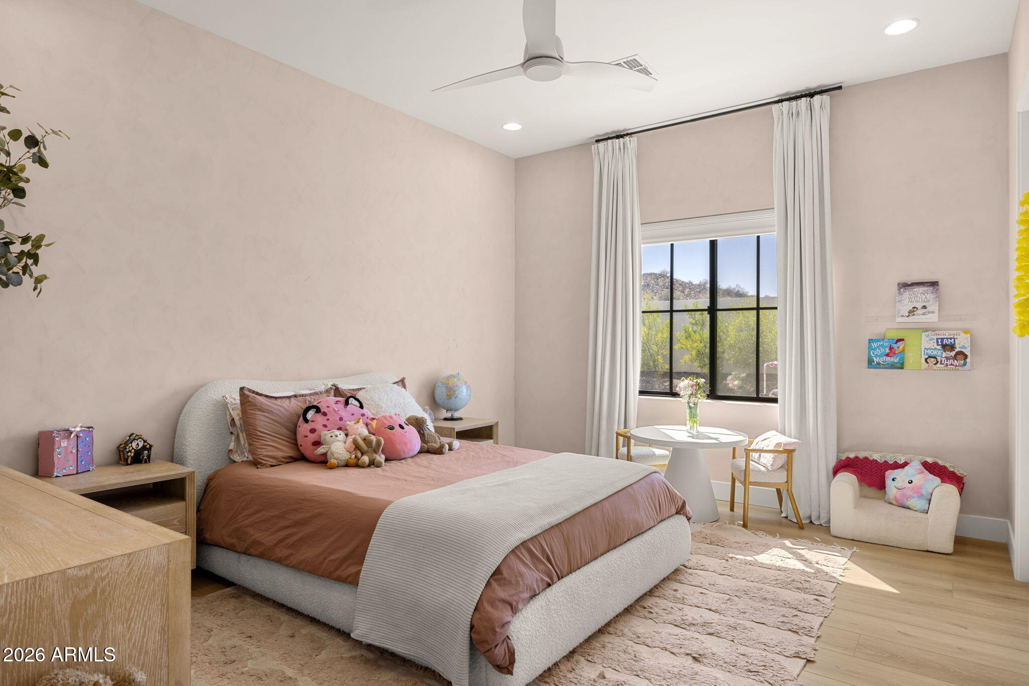 Furnished bedroom with a rose-colored bed, plush toys, and a large curtained window.