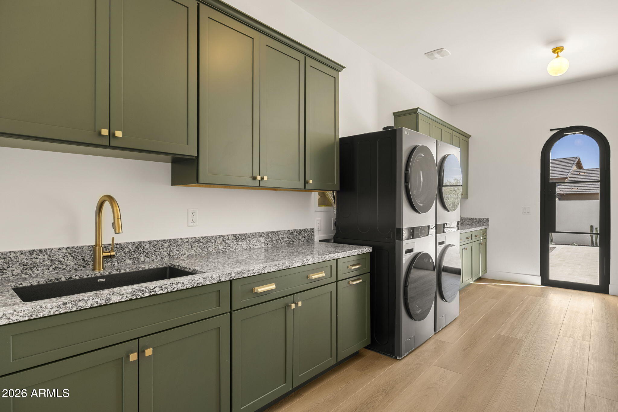 Laundry room with green cabinetry, a speckled stone counter, stacked washer and dryer, and an arched patio door.