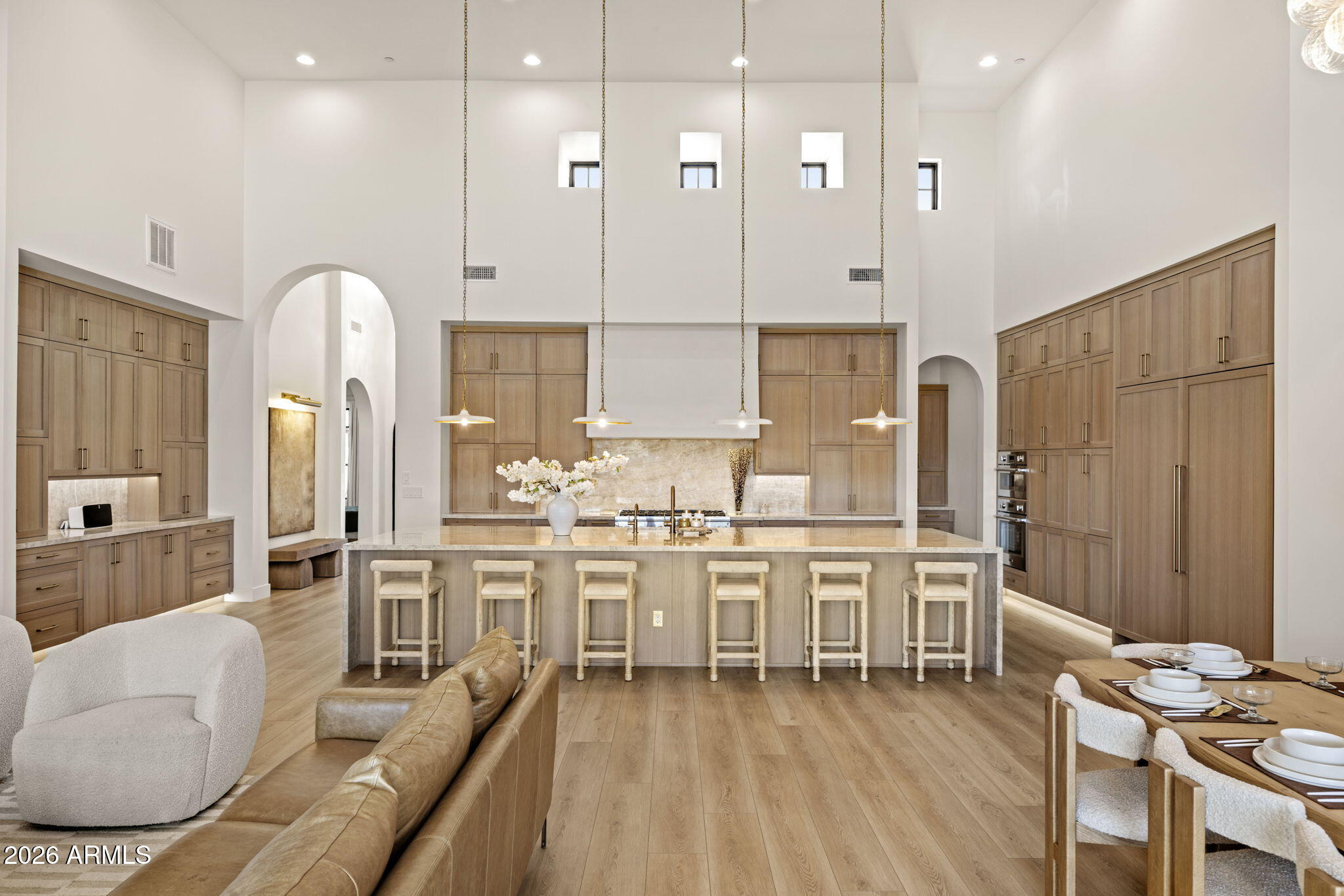 Double-height kitchen with wood cabinetry, a large island, six stools, and an adjoining dining area.