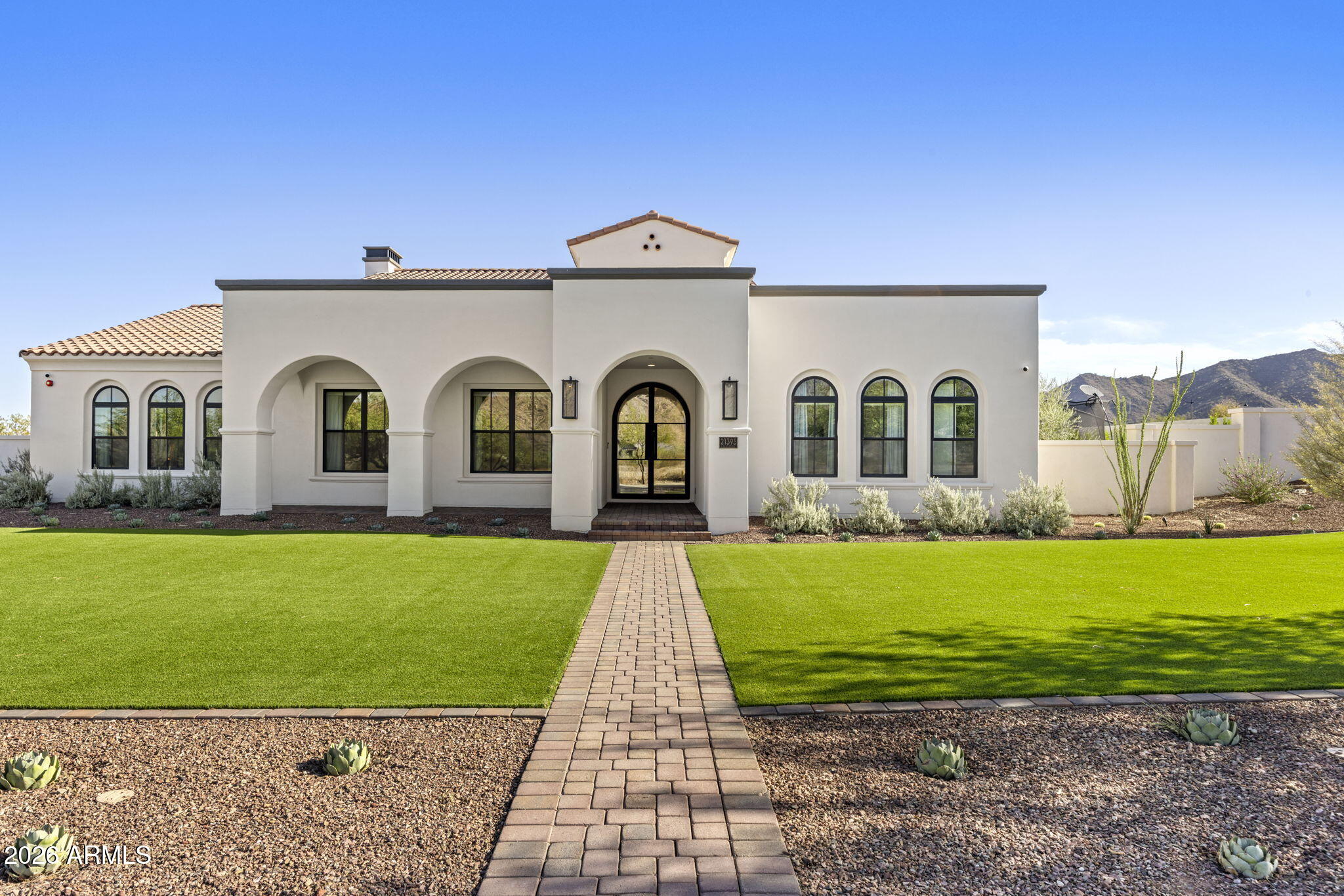 White stucco home with arched windows, green lawn, and a central paver walkway.