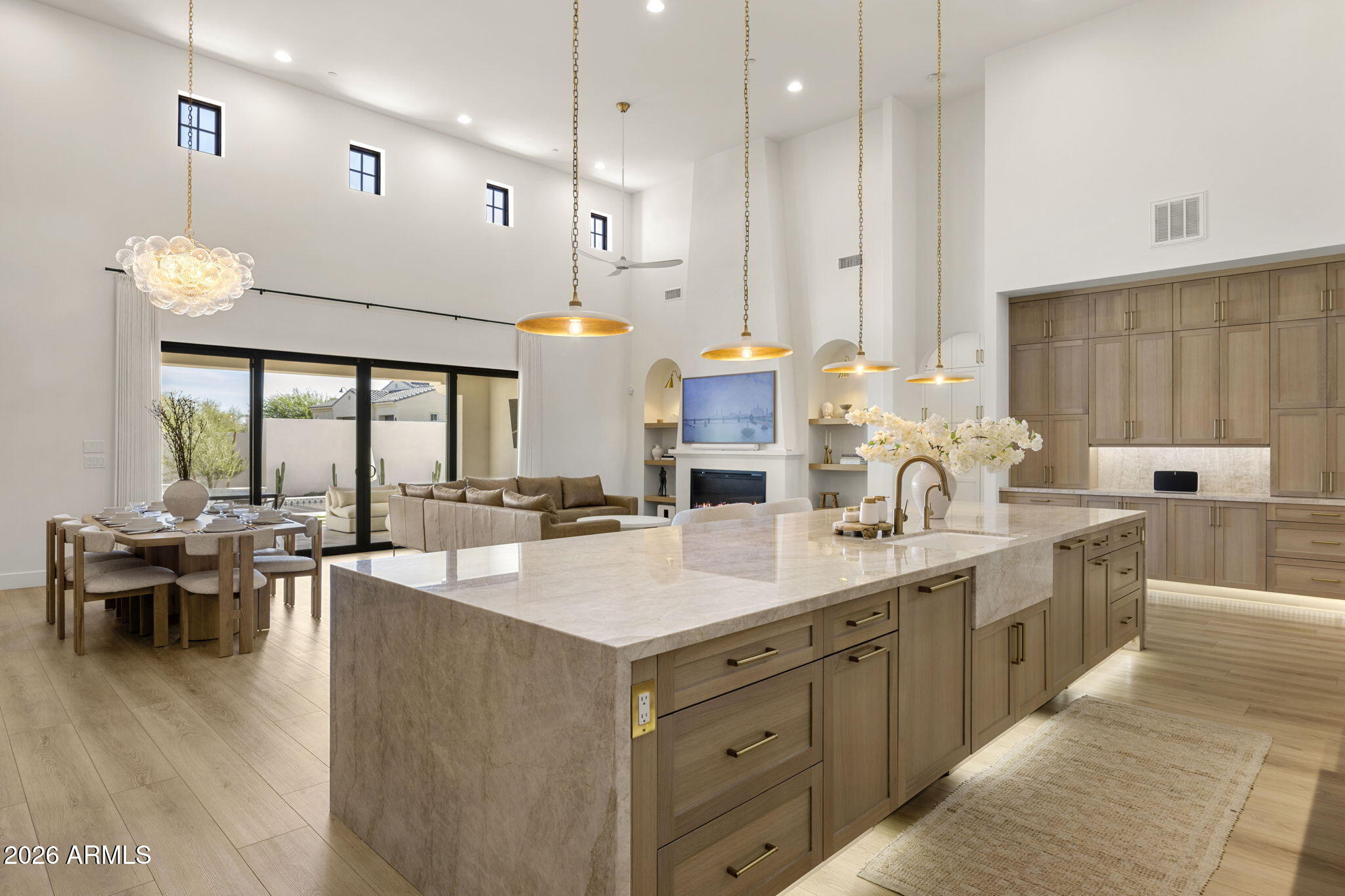 Open-plan kitchen with a large stone island, light wood cabinets, and adjoining dining and living areas.