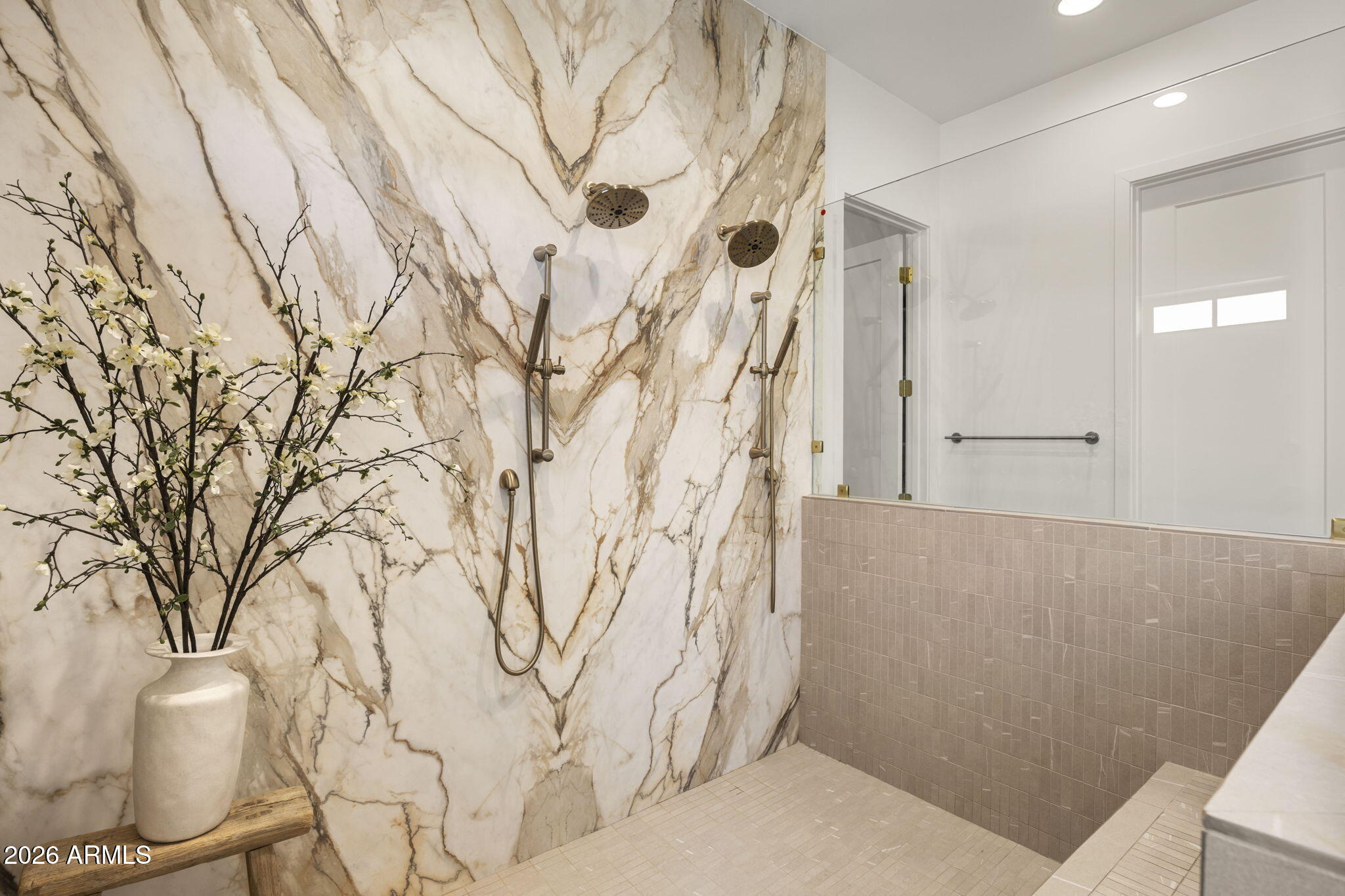 Walk-in shower with dramatic veined marble walls, bronze fixtures, and clear glass enclosure.