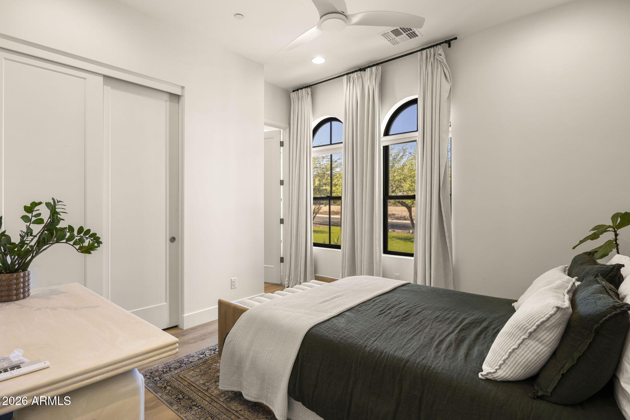 Furnished bedroom with a dark bed, two arched windows, and long white curtains.