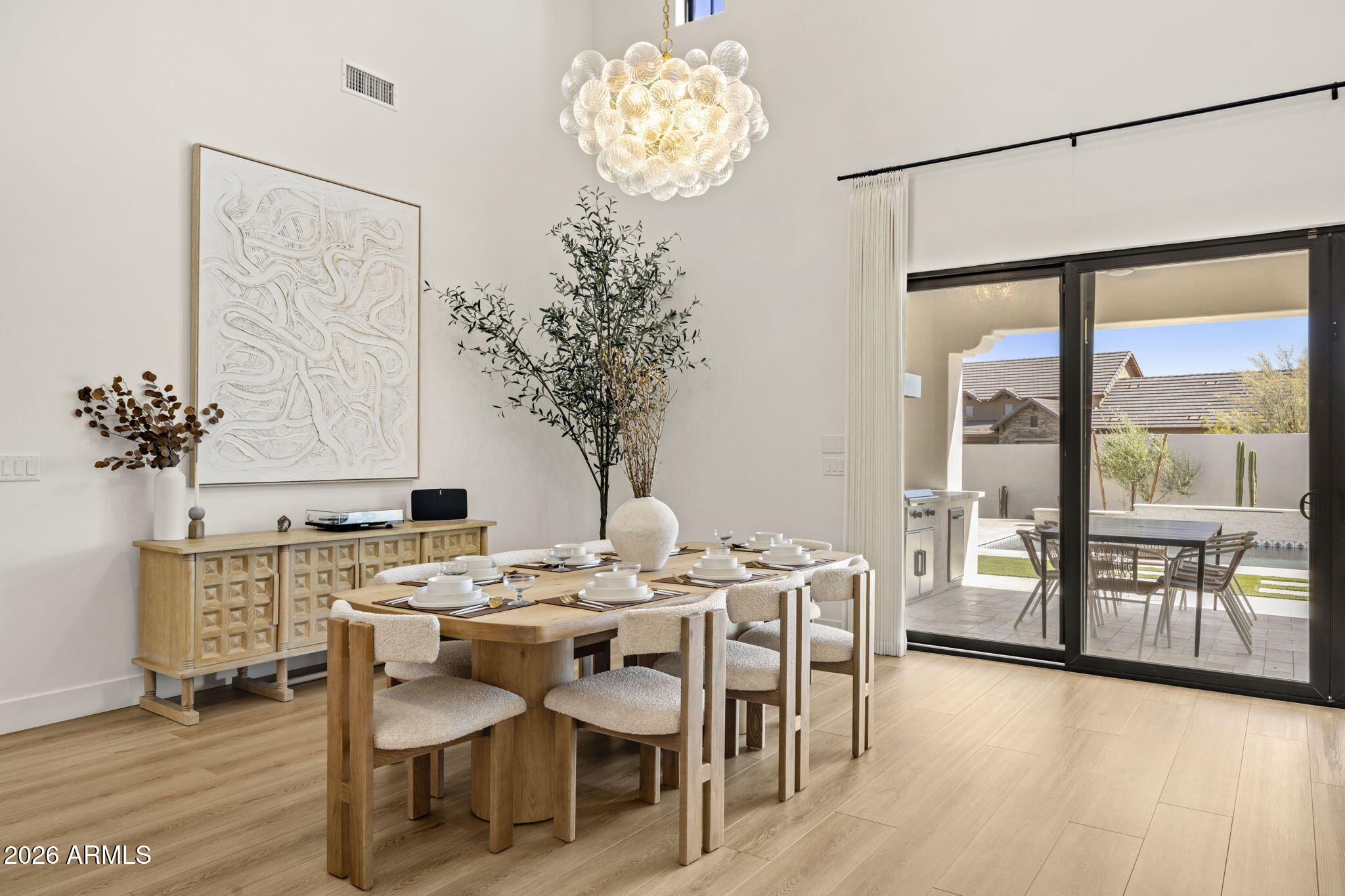 Dining room with a set wooden table and sculptural chandelier beside sliding doors to a patio and pool.