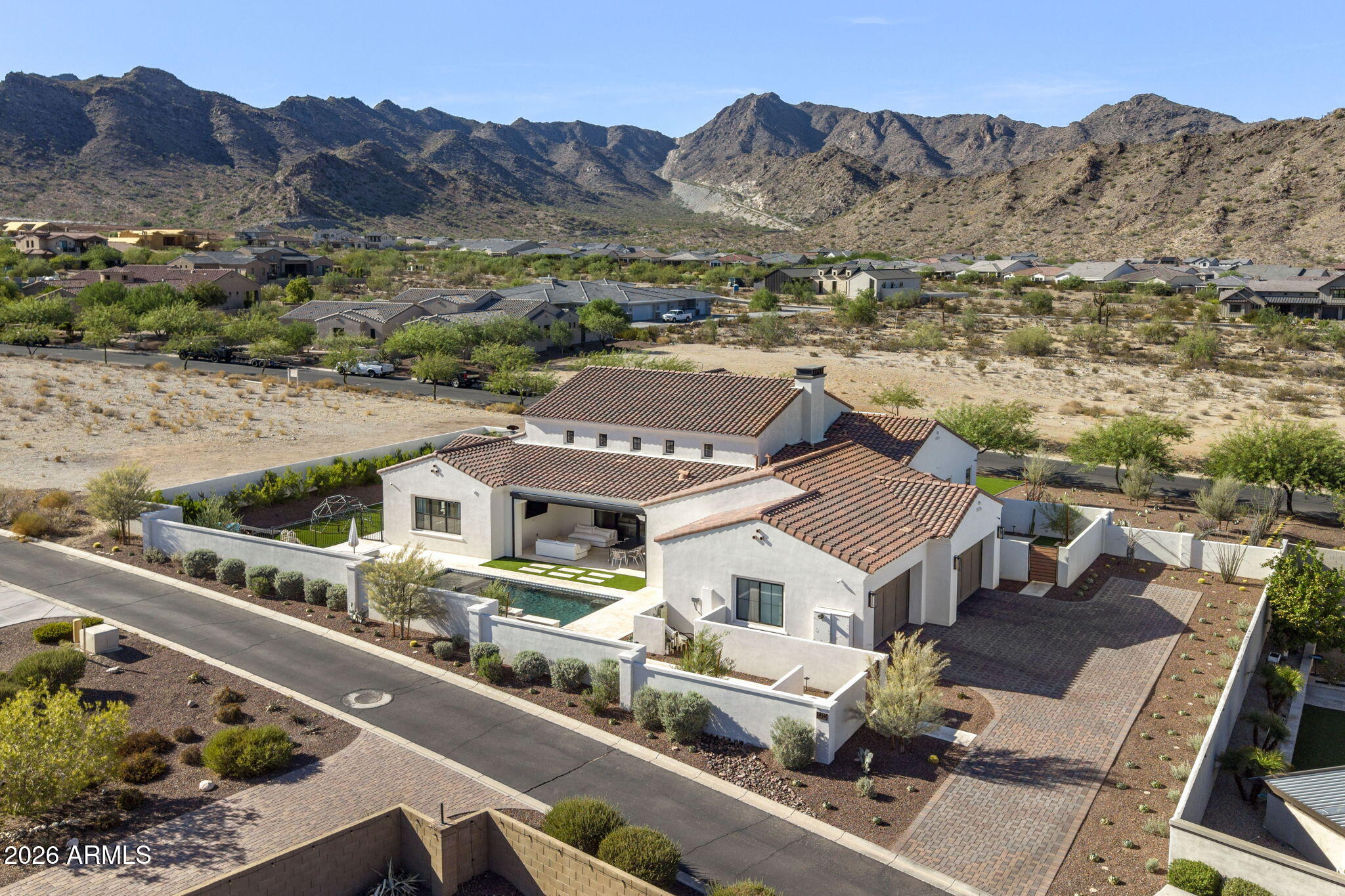 Aerial view of a white stucco home with a pool, walled courtyard, and mountain backdrop.