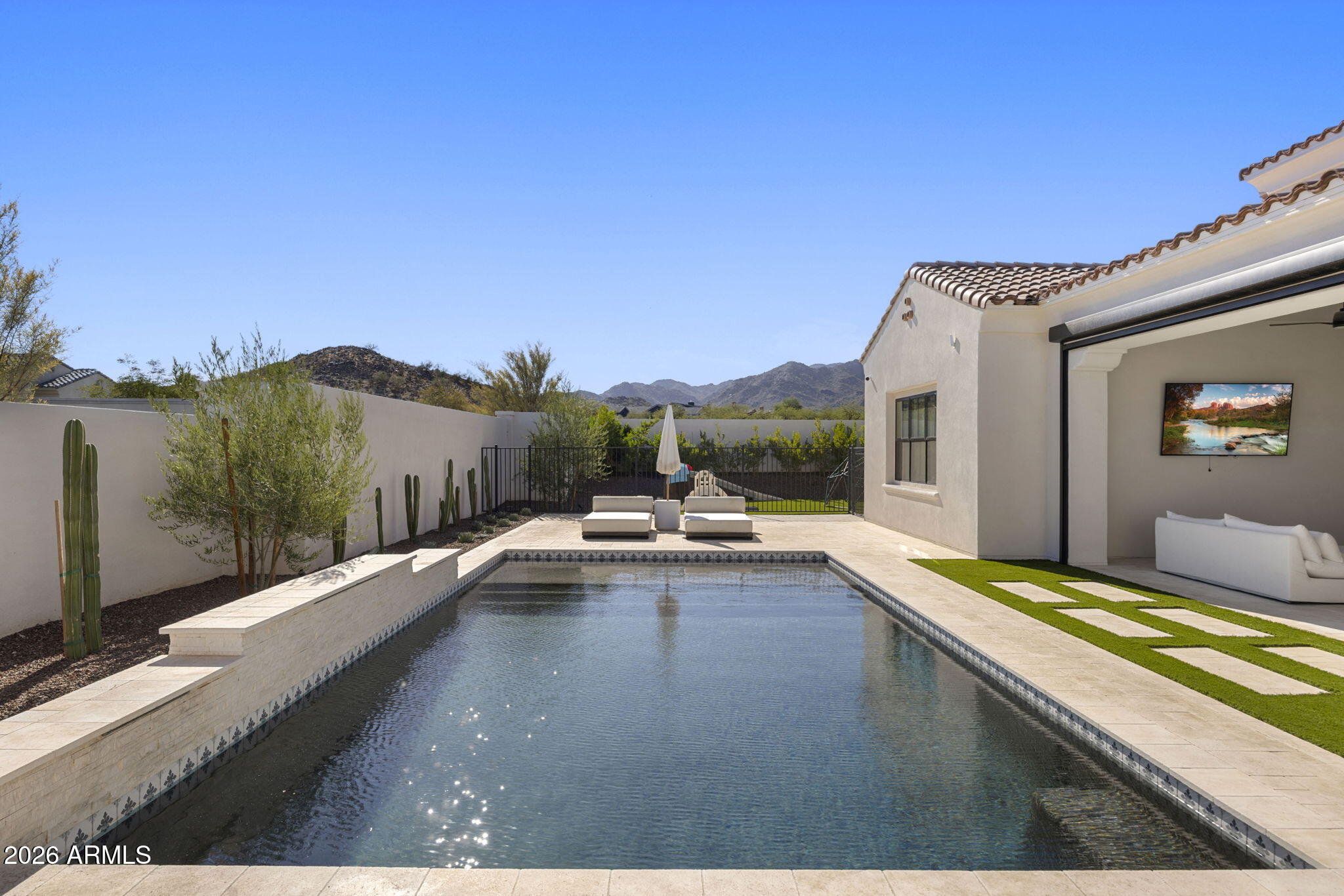 Backyard pool beside a stucco home, with patio seating and mountain views.