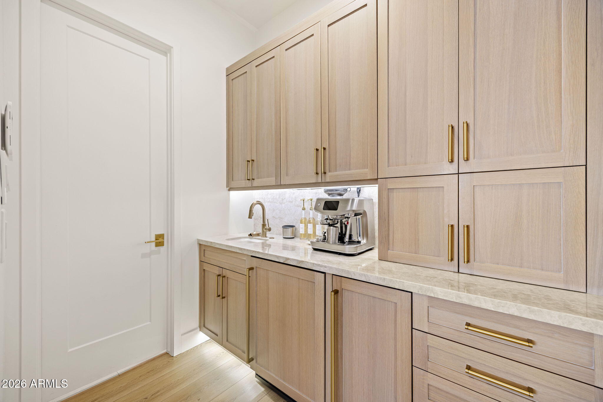 Built-in coffee bar with light wood cabinetry, brass hardware, a sink, and an espresso machine.