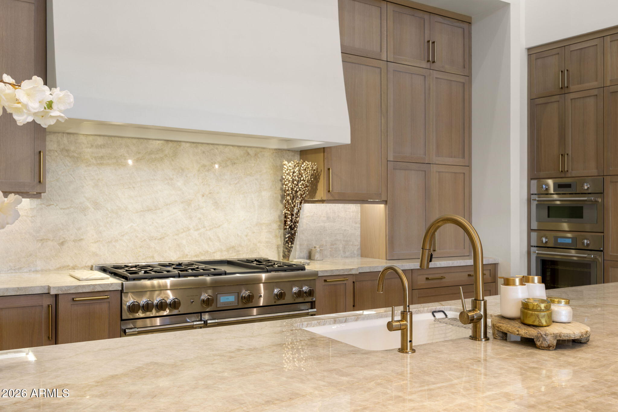 Kitchen with warm wood cabinets, marble surfaces, a large range, double ovens, and brass faucets.