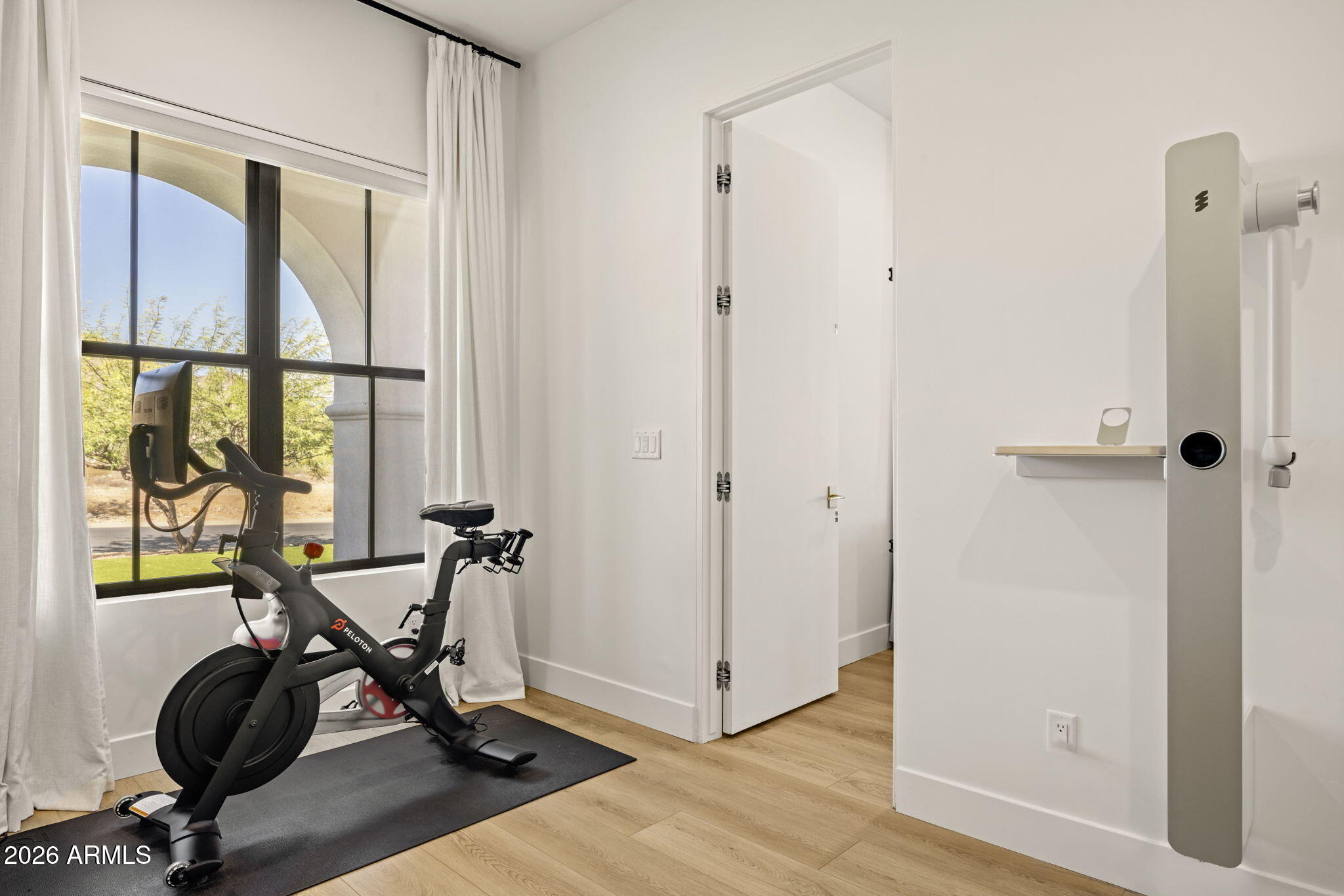 Home workout room with a Peloton bike beside a large window and light wood floors.